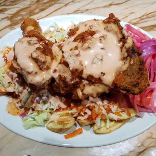 Honduran fried chicken with creamy sauce, cabbage, and pickled red onions on a white plate.