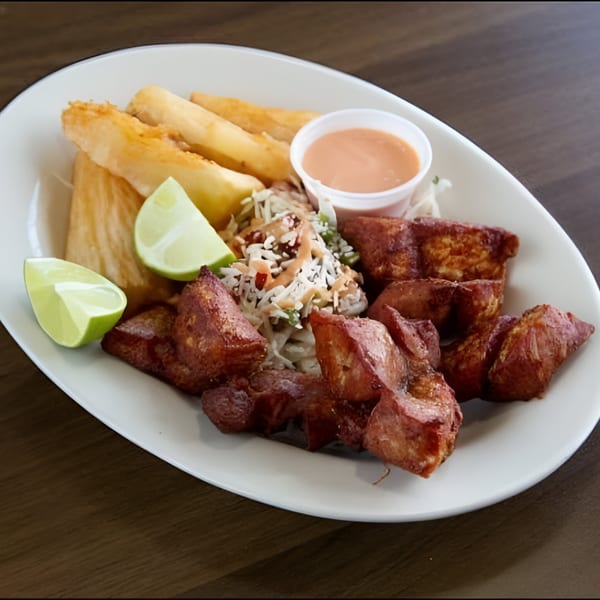 Honduran fried pork chunks with yucca fries, coleslaw, lime wedges, and a dipping sauce.