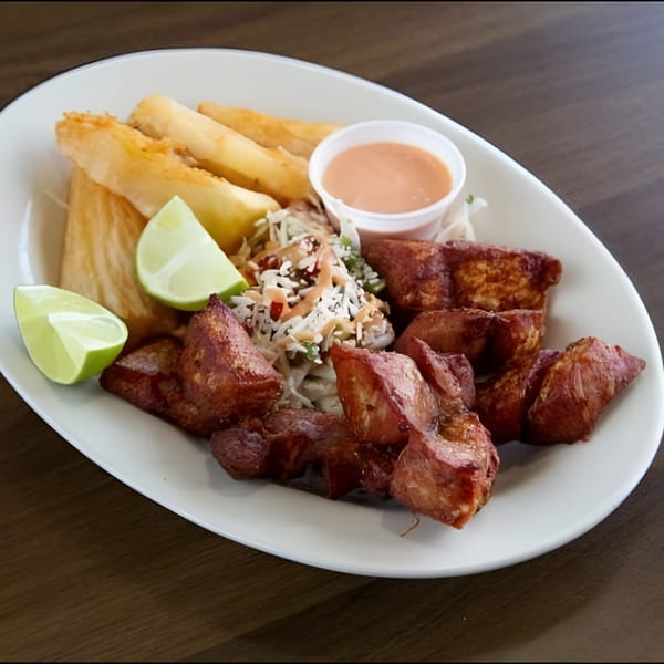 Honduran dish with fried pork, yucca fries, coleslaw, lime wedges, and a side of sauce.