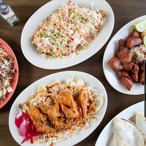 Overhead view of four plates of Honduran food, including baleadas, fried plantains, and meat dishes.
