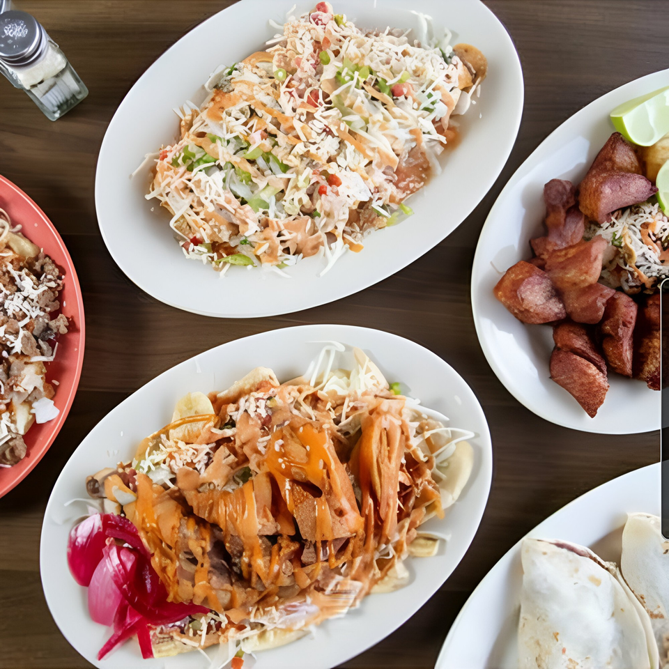 Overhead view of four plates of Honduran food, including baleadas, fried plantains, and meat dishes.