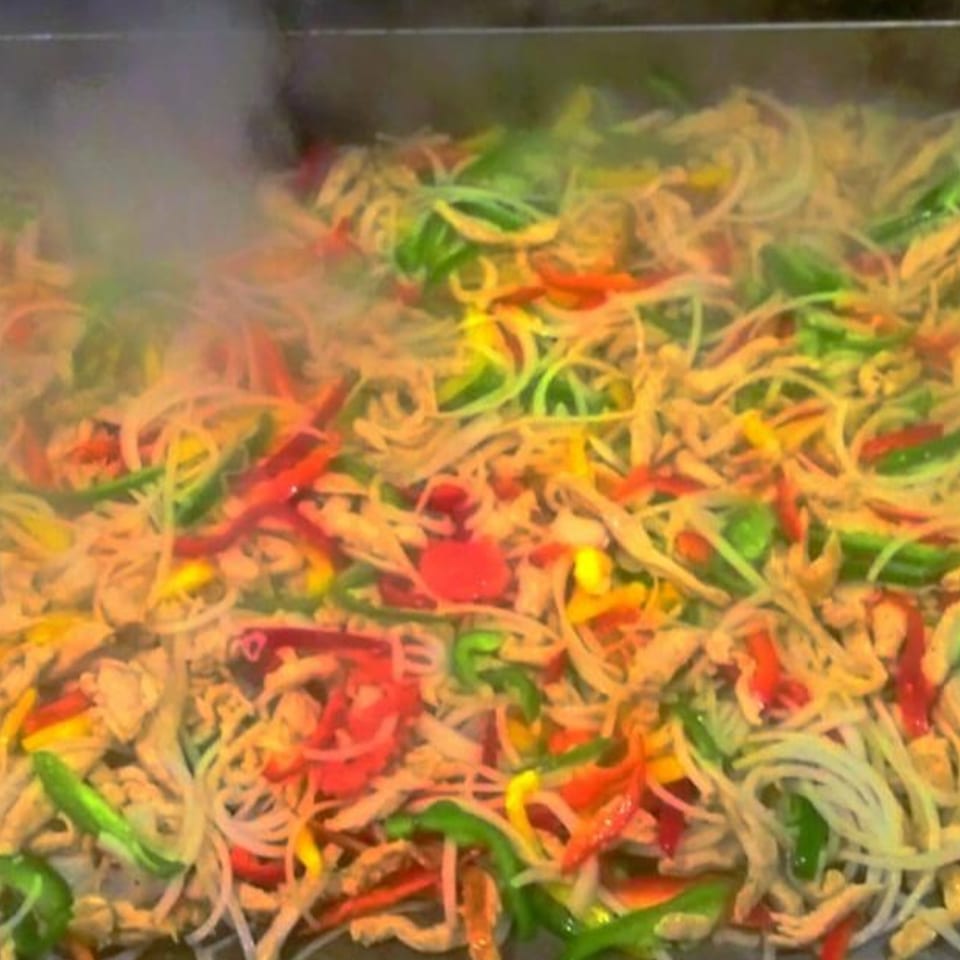Colorful stir-fry with chicken, bell peppers, and onions cooking on a griddle with steam rising.
